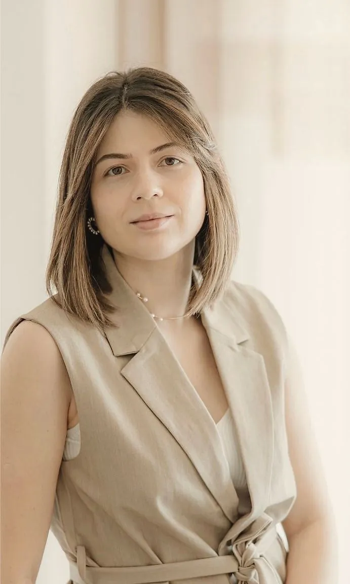 Dra. Marta Fernandes, de fato bege, sentada junto às cortinas